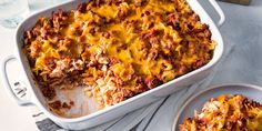 a casserole dish with meat and cheese in it on a table next to two plates