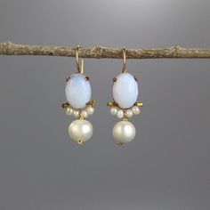 A pair of glowing large clover earrings set with an oval shaped opalite in copper bezel. Beautiful round pearls encircle the lower part of the opalite, and a single large pearl dangles down gently.   The hook is made of gold filled.  This unique design is timeless, so you can enjoy it for years and years to come and pass it on.  Measurements: Opalite in diameter: 10/14mm Total length including the hook: 3.5cm Materials: Stones: opalite, pearls Metal: gold filled, copper bezel  Since I use mostly natural gemstones, each jewel is unique and has its special, magical touch. Therefore, please expect subtle differences in color and form.  Click here for more earrings: https://www.etsy.com/shop/yifatbareket?ref=hdr_shop_menu§ion_id=5891684 TURNAROUND TIME & SHIPPING  This piece will be made withi Oval Opal Jewelry With Matching Earrings, Elegant Handmade Oval Pearl Earrings, White Oval Earrings For Wedding, Oval Pearl Drop Jewelry, White Opal Drop Earrings, Oval Opal Earrings For Formal Occasions, White Oval Earrings With Ear Wire, Oval White Pearl Earrings, Handmade White Oval Earrings