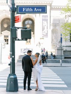 a bride and groom kissing under a street sign in front of a building on fifth avenue