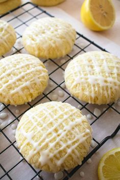 lemon cookies with white icing on a cooling rack next to some sliced lemons