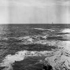 an old black and white photo of the ocean with waves crashing on rocks in the foreground