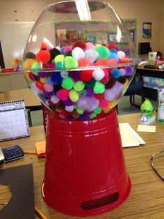 a red gummy machine filled with lots of colorful pom - poms on top of a wooden table