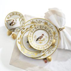 two white and gold plates with birds on them sitting on top of napkins next to each other