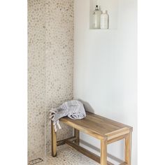 a wooden bench sitting next to a white wall with a towel on top of it