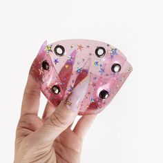 a hand holding up a pink object with black eyes and stars on it's side