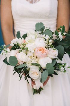 a bridal holding a bouquet of white and pink flowers with greenery on it