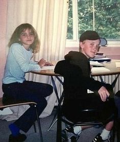 two young children sitting at desks in front of a window, one boy is smiling