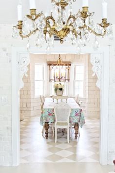 a chandelier hangs over a dining room table in front of a white brick wall