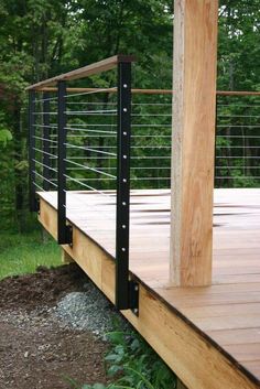 a wooden deck with metal railings in front of some trees and grass on the ground