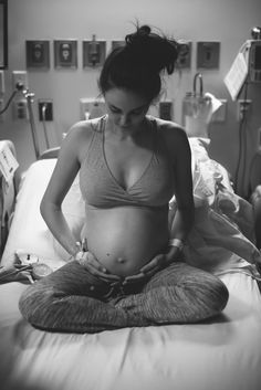 a pregnant woman sitting on top of a bed in a hospital room while holding her stomach