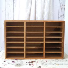 a wooden book shelf with several compartments on top of it, sitting on a table next to a white curtain