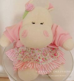 a stuffed animal in a pink dress sitting on top of a glass table with a white wall behind it