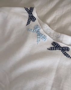 an embroidered white shirt with blue bows on the front and back, sitting on a bed