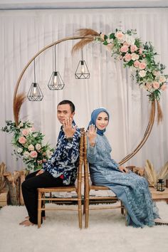 a man and woman sitting on a bench in front of a floral arch with flowers