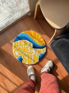 someone standing on the floor in front of a door mat that says here comes the sun