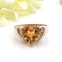 This beautiful honey yellow citrine and diamond ring is solid 14k yellow gold. There are 10 diamonds - 5 on each side of the citrine. They are channel set.  Ring Size: 7.5 - can be sized Metal Content: 14k yellow gold Gemstone: Trillion Cut Citrine Carat: 3 ct Size in mm: 10 x 10 x 6.38 Diamonds: 10 Round Brilliant Cut diamonds Carat: .10 ctw Clarity: SI2 Color: H/I Measurements: Face of Ring (North South): 11mm  Height of ring off of finger: 8mm Band / Shank Width: 2mm Weight: 4.9 Grams Stamps: P14k  Condition: Excellent Estate Items will ship in gift box or pouch Each piece is thoroughly examined and refinished as needed by our professional jewelers, tested to guarantee metal content,  graded by our in-house GIA (Gemological Institute of America) Graduate Gemologist, and inspected for qu Citrine Diamond Ring With Accent Stones In Yellow Gold, Yellow Gold Citrine Diamond Ring With Accent Stones, Yellow Gold Citrine Diamond Ring With Accents, Yellow Gold Diamond Ring With Citrine Accents, Fine Jewelry Citrine Diamond Ring With Accent Stones, Yellow Gold Citrine Jewelry With Diamond Accents, Fine Jewelry Citrine With Diamond Accents, Orange Diamond Accented Jewelry For Weddings, Orange Diamond Jewelry With Diamond Accents