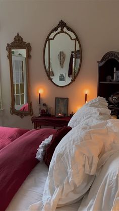 an unmade bed with white sheets and red pillows in front of a mirror on the wall