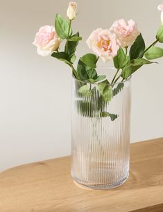 some pink flowers are in a glass vase on a wooden counter top with white walls behind them