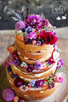 a multi layer cake with fresh fruit and flowers on the top is sitting on a wooden platter