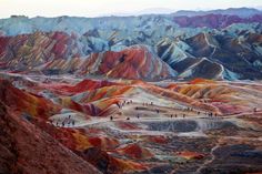 many people are standing on the top of a hill with colorful hills in the background