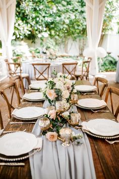 the table is set with white plates and silver napkins, gold chargers and flowers