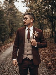 a man in a suit and tie standing on a dirt road with trees behind him