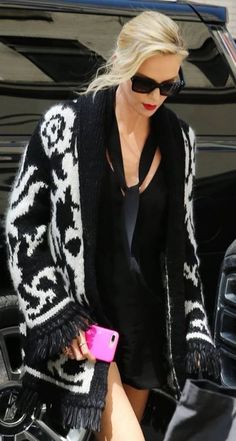 a blonde woman in black and white sweater holding a pink cell phone while standing next to a car