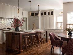 a large kitchen with white cabinets and wooden flooring, along with bar stools