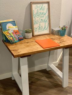 a wooden table topped with a sign next to a potted plant and pencils