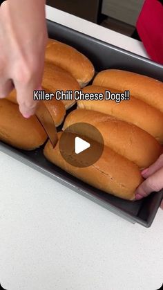 a person cutting bread with a knife on a tray that is filled with buns