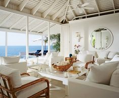 a living room filled with white furniture next to an ocean side house overlooking the water