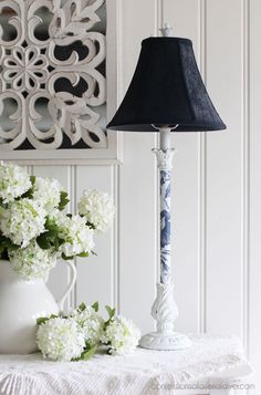 a lamp and vase with flowers on a table in front of a white paneled wall