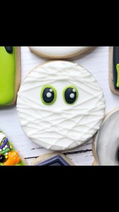 decorated cookies with eyes and mouth on white wooden table top, surrounded by halloween decorations