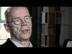 a man with glasses is talking in front of a book shelf and bookshelves