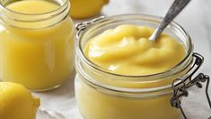 two jars filled with lemon custard on top of a white cloth next to some lemons