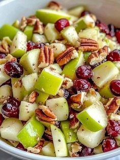 apples, cranberries and pecans are mixed together in a white bowl on a table