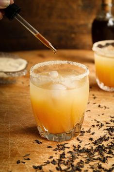 two glasses filled with drinks sitting on top of a wooden table next to bottles and spoons