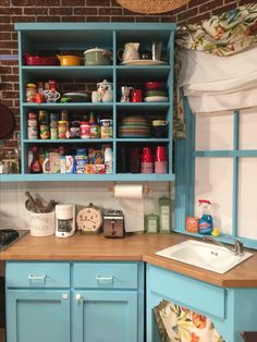 a kitchen with blue cabinets and wooden counter tops in front of a brick wall filled with dishes