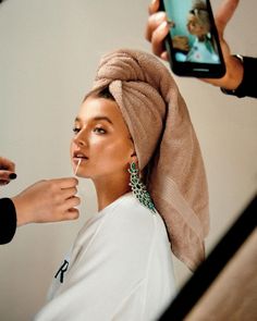 a woman with a towel on her head is getting her makeup done by another person