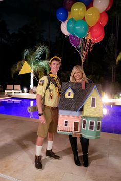 two people standing next to each other in front of a house with balloons on it