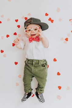 a baby wearing glasses and a bow tie laying on the ground with hearts around him