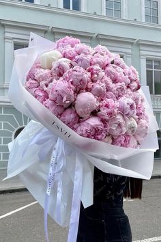 a woman holding a bouquet of pink flowers in front of a white building on the street