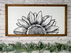 a black and white drawing of a sunflower hangs on a brick wall next to greenery