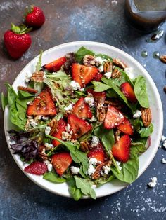 a salad with spinach, strawberries and feta cheese in a white bowl