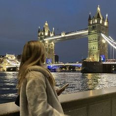 a woman looking at her cell phone in front of the tower bridge