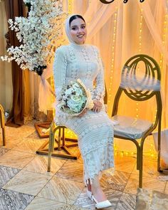 a woman sitting on a chair with flowers in her hand and wearing a hijab