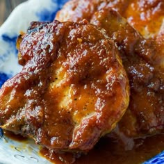 two pieces of meat covered in sauce on a blue and white plate