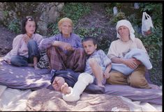 an older woman and two young children sitting on a blanket with their feet propped up