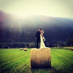 a bride and groom standing on hay bales in the middle of a grassy field