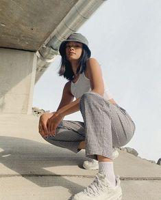 a woman sitting on the ground with her legs crossed wearing white sneakers and plaid pants